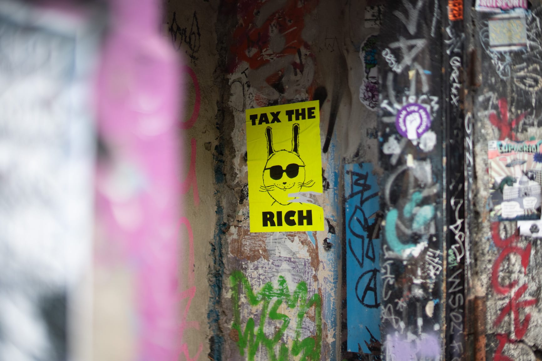 A yellow background poster of a funny crudely drawn rabbit wearing sunnies, and big bold black text in caps reading "tax the rich"